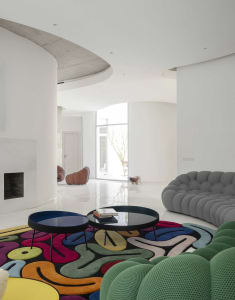 Modern minimalist living room with concrete floors, colorful carpet, and upholstered furniture.