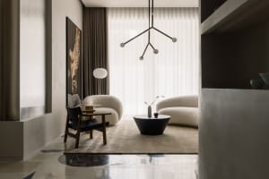 A modern living room with neutral-colored furniture, a round coffee table, and a minimalistic chandelier hanging above the se