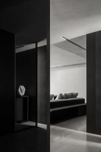 A modern minimalist living room with concrete walls, a built-in sofa, and a minimalist vase on a side table.