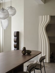 Modern minimalist dining room with a wooden table adorned with decorative vases and contemporary pendant lights.