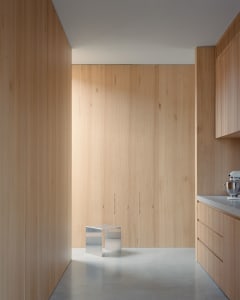 A minimalist kitchen featuring wooden walls and cabinets with a metallic stool in the center.