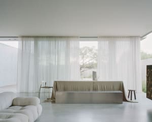 A modern living room with large windows, glass curtains, and concrete furniture.