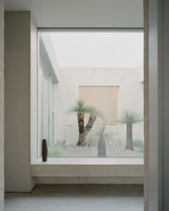 A minimalist living space with a large window showcasing a serene courtyard with palm trees.