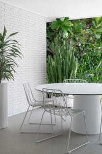 Modern dining room with metallic floor tiles, white brick wall, and large green plants.
