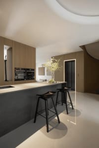 A minimalistic kitchen with concrete flooring and wooden cabinets, featuring a bar area with black stools and a vase of flowe