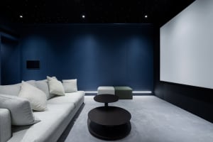 Modern minimalist living room featuring a white sofa with white cushions, a dark round coffee table, and dark blue walls with