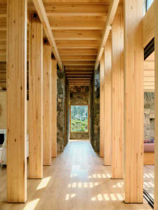 A modern corridor with wooden columns and a stone wall, featuring a window overlooking a natural landscape.
