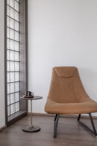 A modern, minimalist living room with a tan leather chair, a small, round side table with a black mug, and a glass block wall
