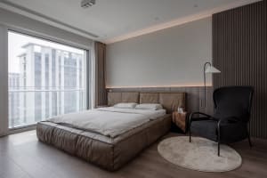 A minimalist bedroom featuring a large bed made of leather, a black armchair, and a round rug.