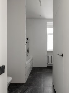 Modern minimalist white bathroom with black marble flooring and white tiled shower area.