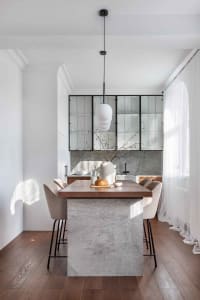 Modern kitchen with wooden dining table and concrete island, featuring a hanging pendant light and beige upholstered chairs.