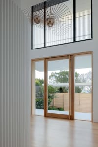 A minimalist living space featuring light-colored wood and glass doors, with a view of a green garden.