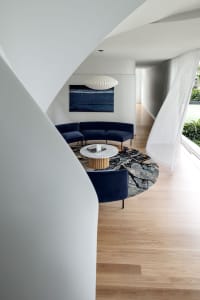 A modern living room with a dark blue fabric sectional sofa, a marble coffee table, and a round rug with a nature-inspired pa