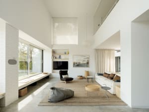 A minimalist residential living room with neutral tones, featuring a white sofa, coffee tables, and a window.
