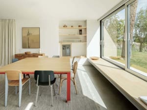 A modern dining room featuring sustainable wooden materials with a red-framed table and colorful chairs.