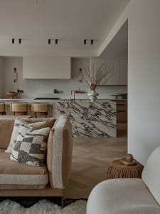 A minimalist residential kitchen features a white marble island with black veins, wooden flooring, and metal kitchen hardware