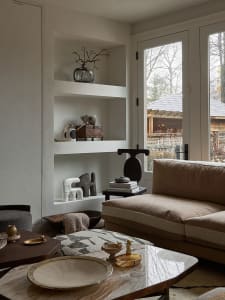An elegant living room with a modern design, featuring a marble coffee table, a comfortable sofa, and decorative shelving.