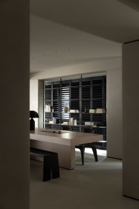 Minimalist modern workspace featuring a wooden table with a bench and black chairs, illuminated by overhead lighting, with a 