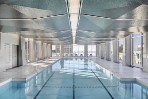 Modern interior of an indoor swimming pool with a glass ceiling and concrete floor, surrounded by tiled walls.