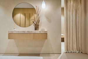 A modern bathroom featuring a marble countertop with a vase of dried plants and a round mirror above it.