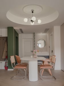 A modern dining room featuring a round white marble table surrounded by orange woven dining chairs.