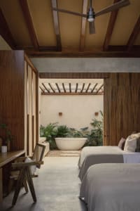 A modern bathroom with a concrete floor and wooden planks, featuring a bathtub surrounded by lush green plants.