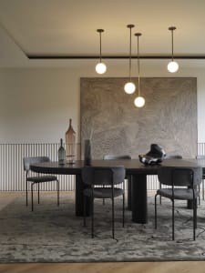 Modern dining room with metallic and glass furniture, pendant lights, and abstract wall art.
