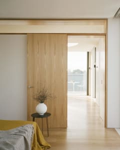 A modern minimalist bedroom with wooden finishes and a vase with dried branches on a small black side table.
