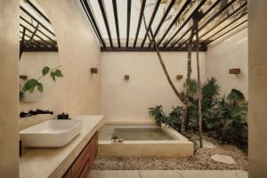 A minimalist bathroom features a bathtub surrounded by plants, with a sink and mirror on the left wall.