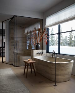 Modern minimalist bathroom featuring a freestanding natural stone bathtub, a glass-enclosed shower, and a wooden stool with a