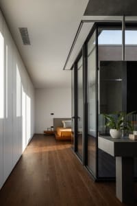 Modern minimalist bedroom featuring dark wood flooring, concrete walls, and a bed with an orange bedspread.