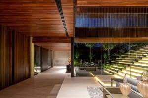 A modern interior living room with glass stairs leading to an outdoor area, featuring soft lighting and minimalist decor.
