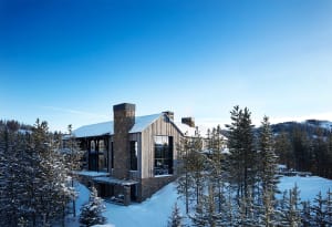 Modern rustic winter lodge with snow-covered trees and blue sky.