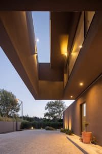 Concrete entrance and pathway leading up to a modern building with a skylight and warm lighting.