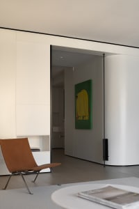 Modern minimalist residential space with white walls, a brown chair, and a green painting.