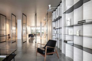 Modern living room featuring minimalist furniture, a sleek black armchair, and a library corner with concrete shelving and gl