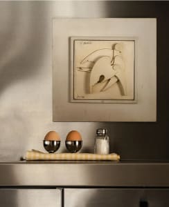 A minimalist kitchen with stainless steel appliances and a decorative bird sculpture on the wall.