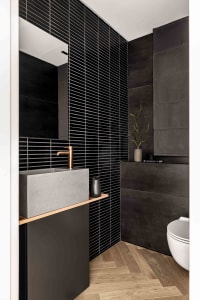 Modern bathroom with black tiles, concrete sink, and wooden flooring.
