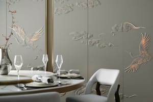 A modern dining room featuring metallic texture wall panels with bird and cloud motifs, table setting, and wine glasses.