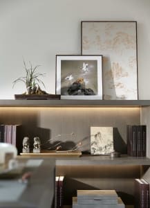A modern shelf decorated with wooden elements, including books, a bonsai plant, and framed art.