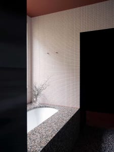 Modern bathroom with a white terrazzo tub surrounded by pink and white checkered tile walls and a black counter