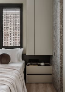 Minimalist bedroom featuring a bed with white bedding and a modern nightstand with a cup and books, set against a terrazzo wa