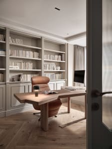 A modern home office featuring a wooden table, leather chair, and full-bookshelves.