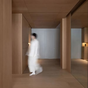 A modern interior space with wooden walls and doors, featuring a blurred figure walking through the corridor.