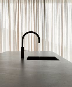 A minimalist modern kitchen featuring a concrete countertop and sink with a black faucet.