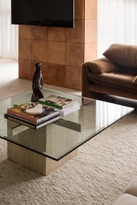 A modern living room with a glass coffee table, concrete furniture, and a brown sofa.