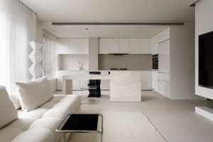 A modern minimalist kitchen with white cabinets, a marble kitchen island, and a white sofa in the foreground.