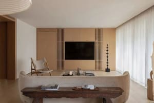 A modern minimalist living room featuring a wooden couch, glass coffee table, and a large window with sheer curtains.