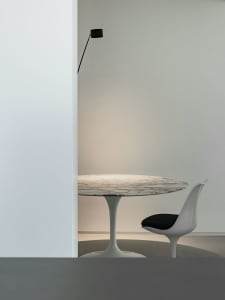 A minimalist modern dining room featuring a round marble table with a sleek, white tulip base and a single white chair with a