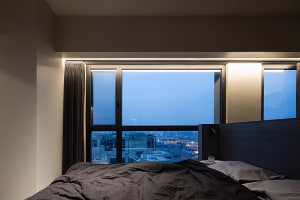 A minimalist bedroom featuring a large glass window overlooking the cityscape.